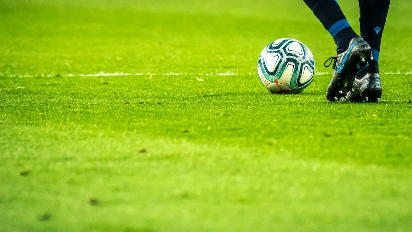 Balón de fútbol junto al pie de un jugador, sobre el césped